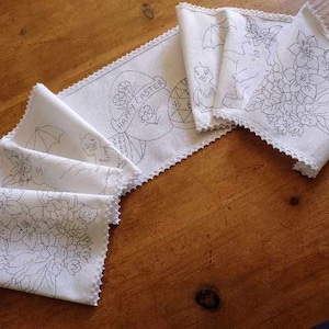 May include: A set of five white embroidered table runners with a scalloped edge. The runners feature different Easter-themed designs, including a bunny, flowers, and an egg with the text "Happy Easter".