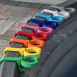 May include: A row of colorful, plastic cup holders in various colors, including green, yellow, orange, red, pink, blue, white, and gray. The cup holders are attached to a dark gray metal bar.