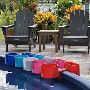 May include: A set of colorful pool cup holders in blue, teal, gray, pink, and red, attached to the edge of a pool. Two dark gray Adirondack chairs and a small table are in the background, suggesting outdoor relaxation.