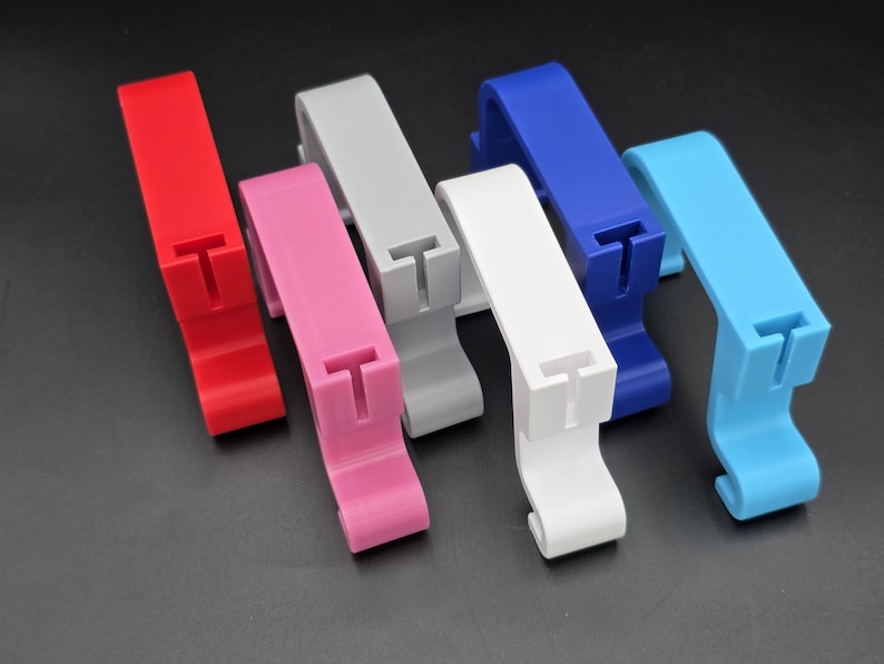 May include: A collection of colorful, plastic clips in red, pink, gray, white, blue, and light blue. Each clip has a T-shaped slot and a curved base. The clips are arranged on a dark surface.
