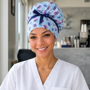 May include: A light blue scrub cap featuring a repeating pattern of colorful retro cassette tapes. The cap has a gathered back design with a dark blue ribbon tied into a bow at the center, providing a secure fit for the wearer's hair.