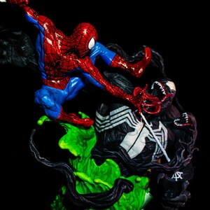 May include: A detailed figurine depicting a battle between Spider-Man and Venom. Spider-Man is in a dynamic pose, clad in a red and blue suit, while Venom, a black symbiote, is in a menacing stance. The base is a vibrant green.