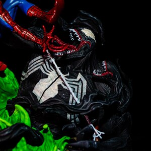 May include: A detailed figurine of Venom in a battle scene with Spider-Man. Venom is predominantly black with white accents and a large, menacing mouth. Spider-Man is in a classic red and blue suit, with his web-shooters visible.