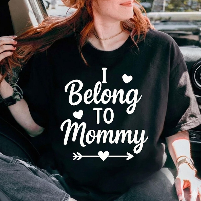 May include: Black t-shirt with the text "I Belong to Mommy" in white script. The design includes hearts and an arrow. A casual, comfortable top for everyday wear.