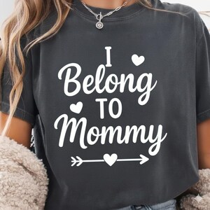 May include: Dark gray t-shirt with the white text "I Belong TO Mommy" in a script font. The design includes heart shapes and an arrow. The shirt is a casual style.