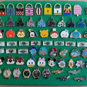 May include: A collection of various Disney-themed enamel pins arranged on a green display board. The assortment includes padlock-shaped pins, castle silhouettes, character faces, miniature license plates, watches, and airplane-shaped pins.