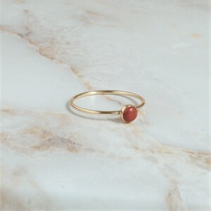 Puede incluir: Un anillo de oro simple con una peque&ntilde;a piedra redonda de color rojo.