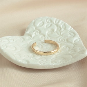 May include: A gold hammered ring on a white heart-shaped dish with a floral design.