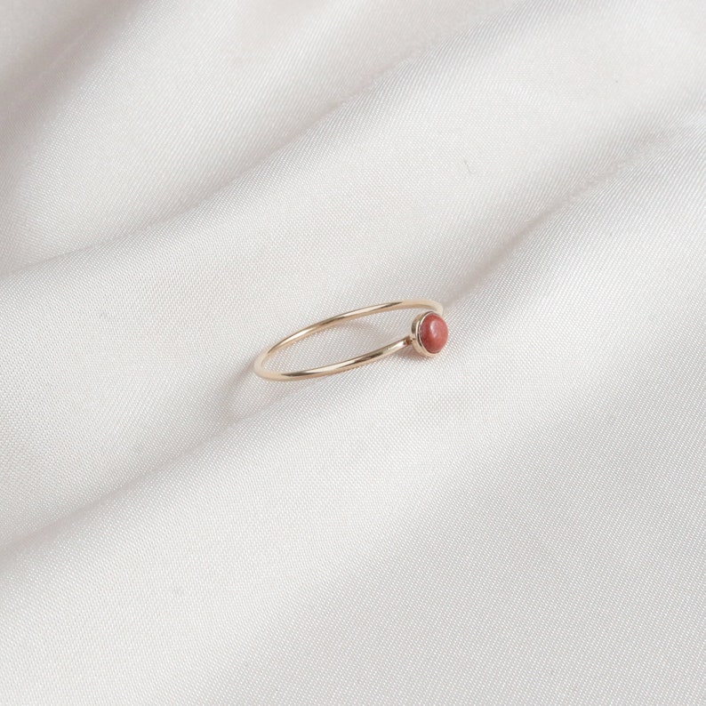 Puede incluir: Un delicado anillo de oro con una sola piedra preciosa redonda de color marr&oacute;n rojizo.