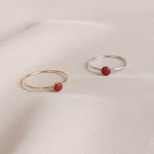 Puede incluir: Dos anillos simples con una piedra preciosa roja engastada en el centro. Un anillo es de oro y el otro de plata.