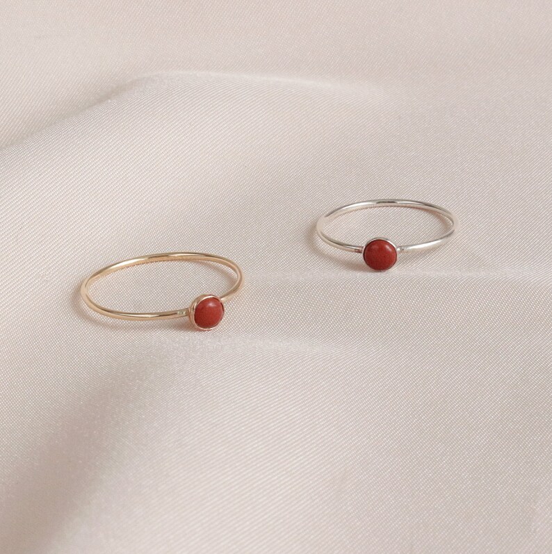 Puede incluir: Dos anillos simples con una piedra preciosa roja engastada en el centro. Un anillo es de oro y el otro de plata.