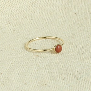 Puede incluir: Un anillo de oro con una sola piedra preciosa redonda de color marr&oacute;n rojizo.