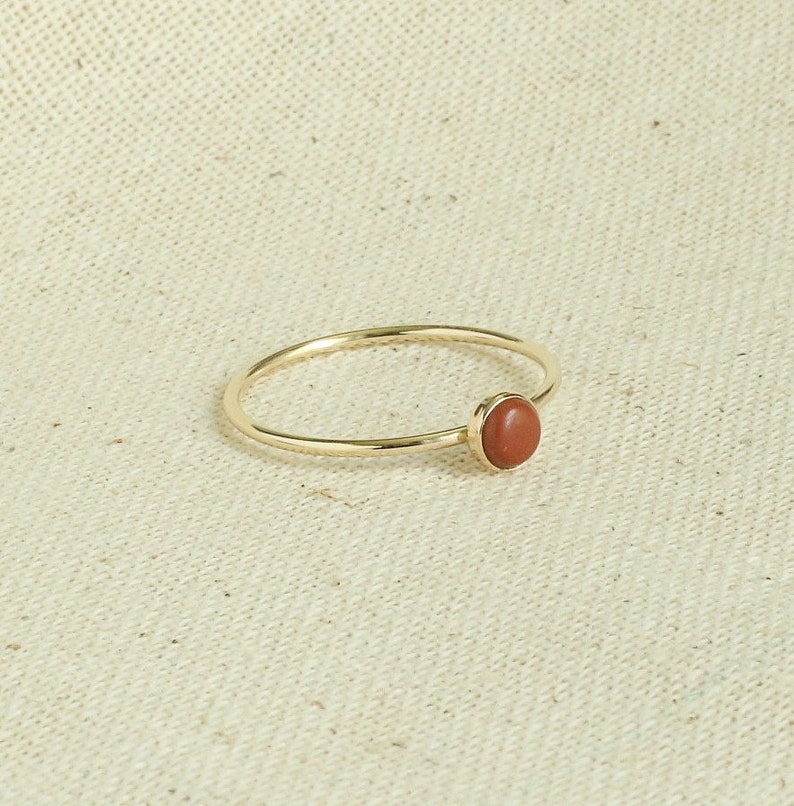 Puede incluir: Un anillo de oro con una sola piedra preciosa redonda de color marr&oacute;n rojizo.