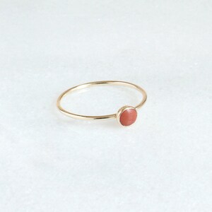 Puede incluir: Un delicado anillo de oro con una piedra redonda de color coral.