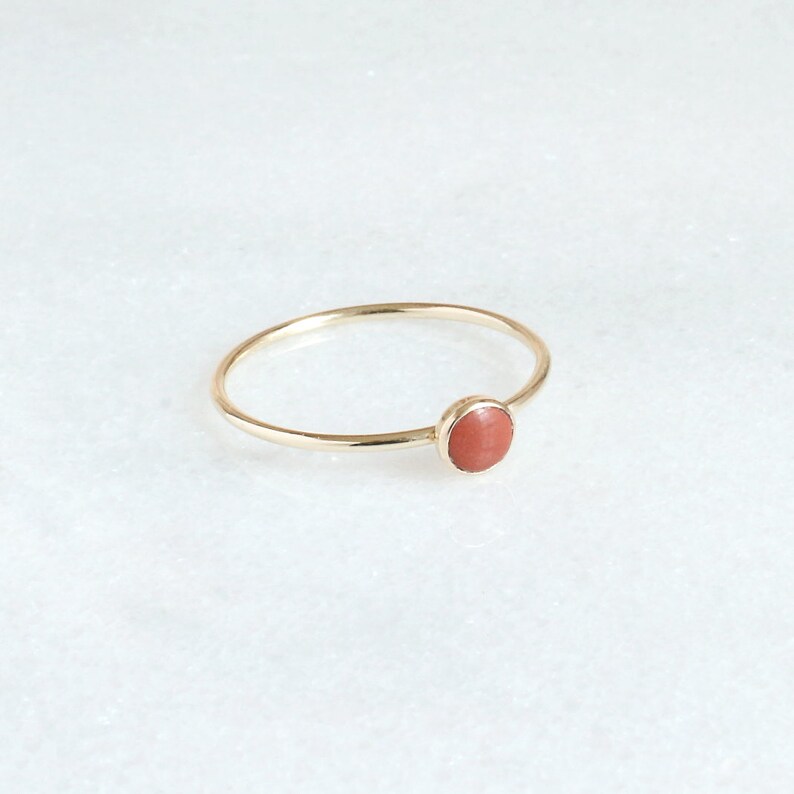 Puede incluir: Un delicado anillo de oro con una piedra redonda de color coral.