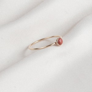 Puede incluir: Un delicado anillo de oro con una sola piedra preciosa redonda de color marr&oacute;n rojizo engastada en la banda.