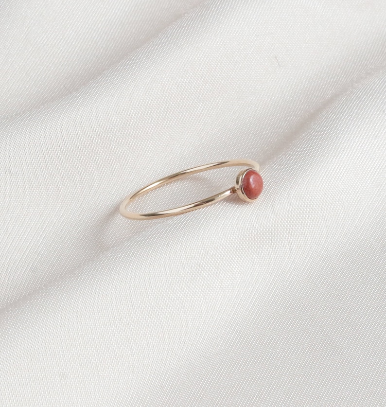 Puede incluir: Un delicado anillo de oro con una sola piedra preciosa redonda de color marr&oacute;n rojizo engastada en la banda.