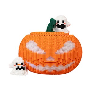 May include: An orange, pixelated jack-o'-lantern with a carved face and a green stem. Two white pixelated ghosts are featured, one inside the pumpkin and one beside it. The Halloween-themed decoration is made of small blocks.