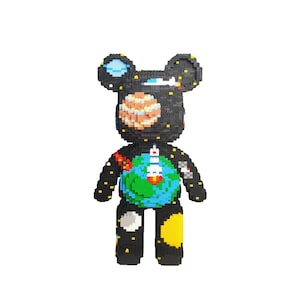 May include: A black bear-shaped figurine constructed from small blocks, featuring a space-themed design. The bear's body showcases a planet Earth with a rocket, a large orange planet, and a starry night sky. Yellow and white accents are scattered throughout.