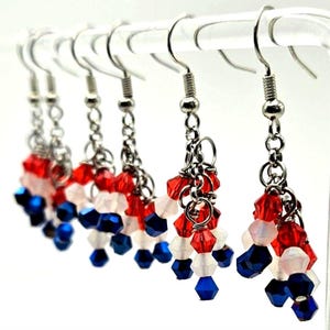 May include: A set of six dangle earrings with red, white, and blue faceted beads. The earrings are suspended from silver-tone hooks and chains. The beads are arranged in clusters, creating a patriotic theme.
