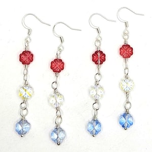 May include: Four pairs of dangle earrings with silver-tone hooks. Each earring features a red flower-shaped bead, a clear bead with yellow accents, and a blue flower-shaped bead. The beads are connected by silver-tone chain.