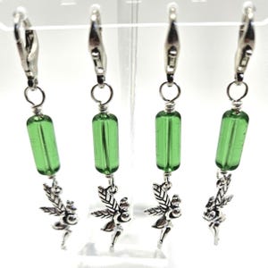 May include: Four silver-toned stitch markers with green glass beads and fairy charms. Each marker has a lobster clasp for easy attachment to knitting or crochet projects. The fairy charms add a whimsical touch.