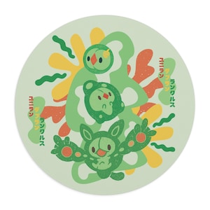 May include: A round, light green graphic featuring three cartoon characters in shades of green, orange, and yellow. The characters are surrounded by abstract shapes and Japanese text. The design is likely for a coaster or sticker.