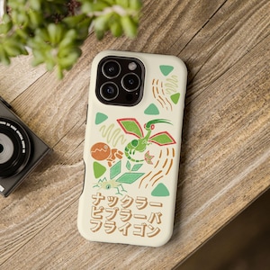 Puede incluir: Funda de teléfono blanquecina con una colorida ilustración de una criatura verde y roja y texto japonés. El diseño incluye acentos naranjas, verdes y marrones. La funda está sobre una superficie de madera con una cámara y una planta en el fondo.