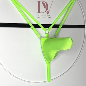 May include: A neon green thong-style garment with a pouch, suspended within a white circular frame. The garment is attached to the frame with thin straps. The text "DV DARK VELVET LEATHER STORE" is visible.