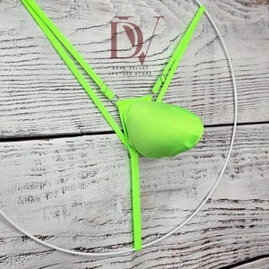 May include: A neon green thong featuring a contoured front pouch and thin adjustable straps. The garment is displayed on a white circular frame. The logo DV LEATHER STORE is visible in the centre, with the text positioned above the pouch.