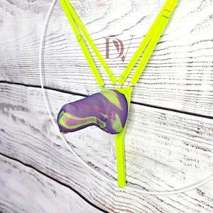 Puede incluir: Un arnés amarillo neón con tiras finas ajustables y una bolsa central con un patrón jaspeado en morado y amarillo neón. El logotipo DV está impreso en el centro. El diseño incluye una tira vertical y dos tiras superiores unidas por anillas metálicas.