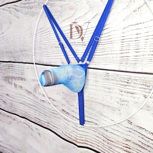 May include: A blue thong featuring thin adjustable straps with silver-toned metal sliders and a central pouch with a marbled blue and white pattern. The garment is displayed on a white circular frame with the logo DV Dark Velvet Leather Store.