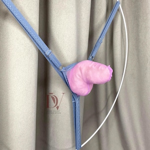 Puede incluir: Un tanga azul claro con un dise&ntilde;o anat&oacute;mico rosa y afelpado. El tanga presenta tirantes ajustables y un panel de malla. El producto se muestra sobre un fondo neutro.