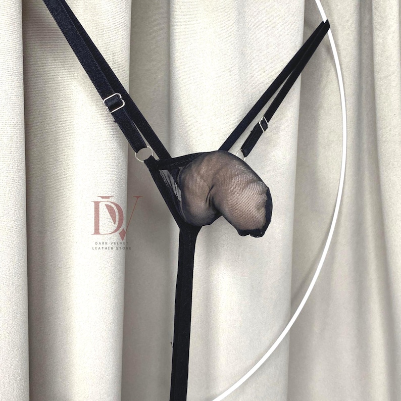 Puede incluir: Lencer&iacute;a negra de malla y tirantes con correas ajustables y herrajes met&aacute;licos. La lencer&iacute;a presenta un dise&ntilde;o de bolsa y est&aacute; suspendida sobre un fondo neutro. El logotipo "Dark Velvet Leather Store" es visible.