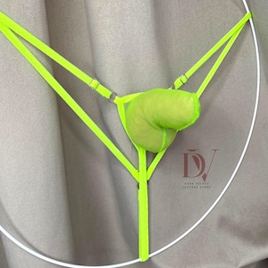 Puede incluir: Tanga de color verde ne&oacute;n brillante con una bolsa de malla y correas ajustables. La lencer&iacute;a est&aacute; suspendida sobre un fondo neutro. El logotipo de Dark Velvet Leather Store es visible en la esquina inferior derecha.