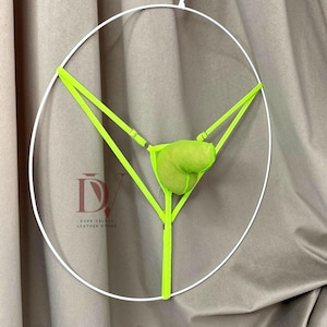 Puede incluir: Conjunto de lencer&iacute;a verde ne&oacute;n con un dise&ntilde;o &uacute;nico, suspendido dentro de un marco circular blanco. El conjunto incluye una braguita tipo tanga y una bolsa a juego. El texto "DARK VELVET LEATHER STORE" est&aacute; presente.