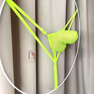 Puede incluir: Conjunto de lencer&iacute;a verde ne&oacute;n con braguita tipo tanga y top en forma de bolsa. El conjunto est&aacute; hecho de un material similar a una malla y tiene correas ajustables. El fondo es de color neutro.