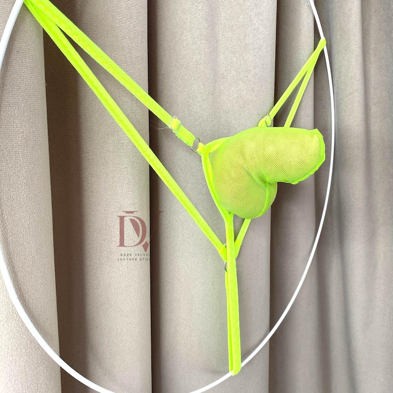 Puede incluir: Conjunto de lencer&iacute;a verde ne&oacute;n con braguita tipo tanga y top en forma de bolsa. El conjunto est&aacute; hecho de un material similar a una malla y tiene correas ajustables. El fondo es de color neutro.