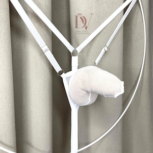 Puede incluir: Conjunto de lencer&iacute;a blanco con dise&ntilde;o de arn&eacute;s, correas ajustables y herrajes met&aacute;licos. Incluye una bolsa suave y acolchada. El logotipo de Dark Velvet Leather Store es visible en el fondo.