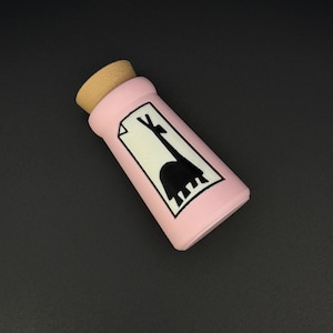 May include: A pink bottle with a cork stopper, featuring a black and white illustration of a giraffe. The bottle is rectangular and appears to be made of ceramic or glass. The giraffe illustration is on a white background.