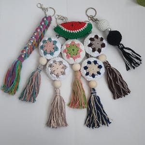 May include: A selection of handmade keyrings with diverse designs. The keyrings feature crochet circles with floral patterns, a watermelon slice, and beaded details. Each keyring has a tassel made of colourful yarn and a silver-coloured metal clasp.