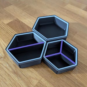 May include: A set of three connected hexagonal trays in dark grey with light grey rims. One tray is open, one is divided into two sections by a purple divider, and one is divided into three sections by a purple Y-shaped divider.