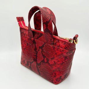 May include: A red snakeskin-effect tote bag with a rectangular shape. The bag features two short handles and a red zip closure. The interior lining is red, and the hardware is gold-coloured.