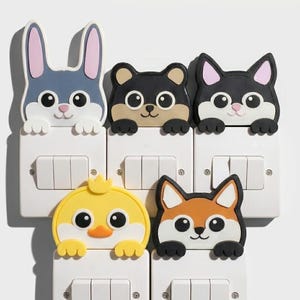 May include: A set of five silicone light switch covers featuring cartoon animal designs including a blue rabbit, a black bear, a black and white cat, a yellow chick, and an orange fox, each with paws resting on the top edge of the white switch plate.
