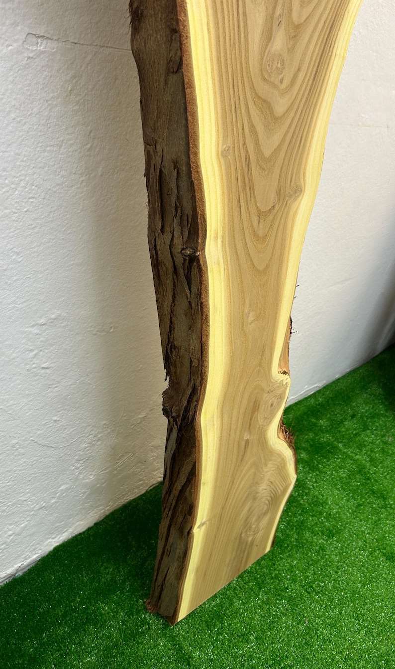 May include: A live edge wood slab with a natural bark edge. The slab has a light brown color with a yellow-toned interior. The wood grain is visible. The slab is approximately 30 inches long.