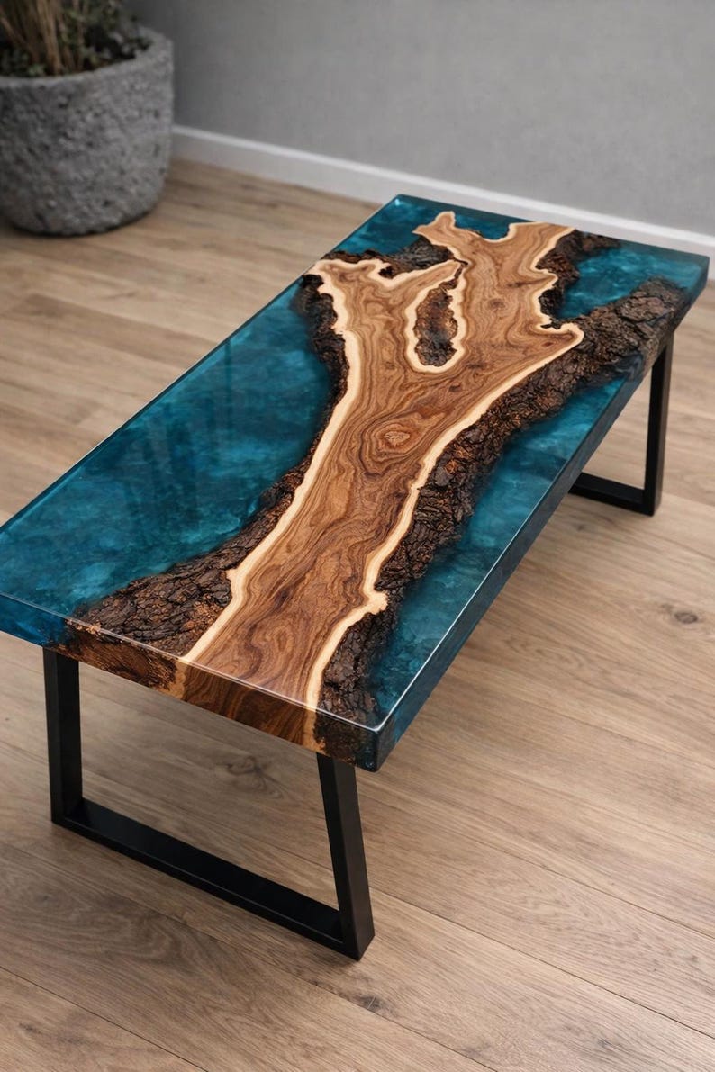 May include: A rectangular coffee table with a unique design. The table features a wooden centerpiece with a natural, organic shape, encased in a clear, turquoise-colored resin. It rests on a black metal frame, creating a modern aesthetic.