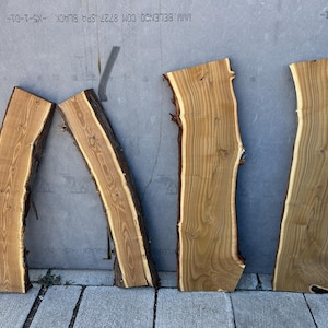 May include: Four irregularly shaped, unfinished wood slabs with natural edges. The wood has a light brown color with darker brown edges and visible grain patterns. The slabs are arranged against a gray background, showcasing their unique shapes and textures.