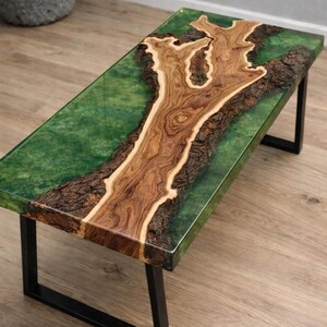 May include: A rectangular coffee table with a unique design. The table features a wooden centerpiece with a natural tree-like pattern, encased in a clear green resin. It rests on black metal legs, creating a modern and artistic aesthetic.