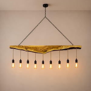 May include: A linear chandelier featuring a natural live-edge wooden beam suspended by two black metal chains. Nine pendant lights with black sockets and tan fabric cords hang from the beam, each fitted with a glowing, warm-toned Edison bulb.