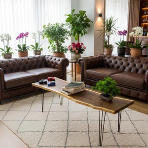 May include: A living room scene featuring brown leather Chesterfield sofas, a wooden coffee table with black hairpin legs, and a cream-colored rug. The room is decorated with potted plants and flowers, creating a warm and inviting atmosphere.